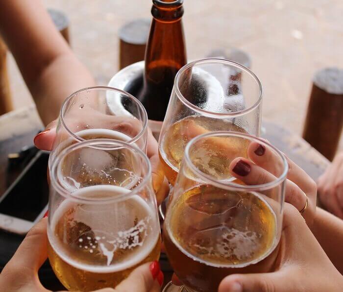 Four clear stem glasses containing beer