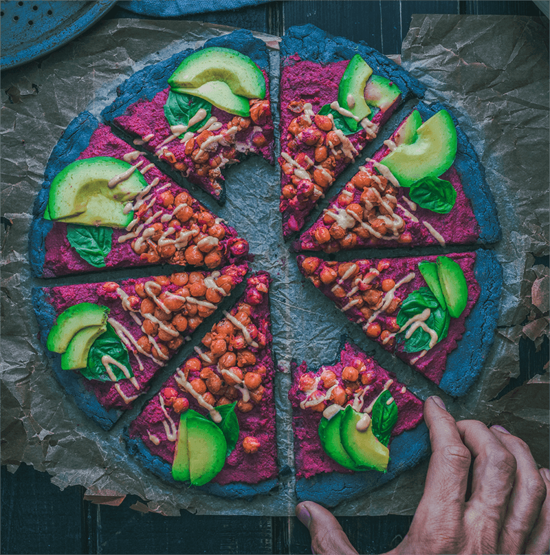 Blue coloured pizza with avocado and spinach