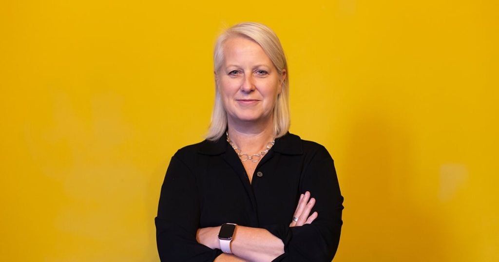 Sarah standing with arms folded in front of a yellow backdrop