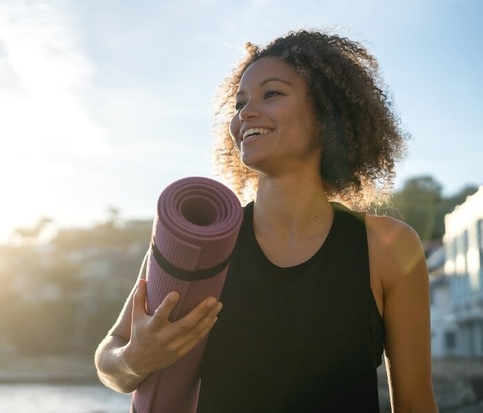 Fit woman holding a yoga mat at the beach