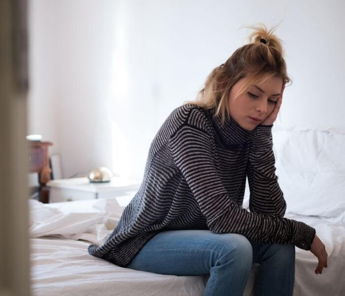 Woman sat on bed looking tired