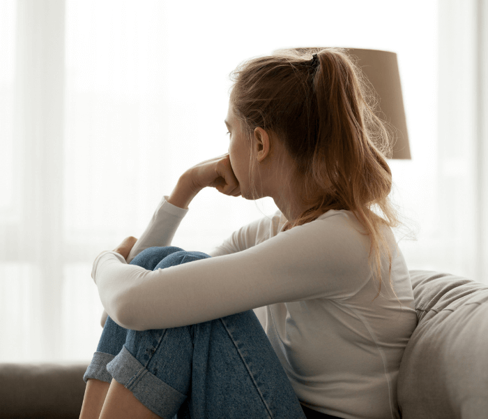 Woman sitting on a couch with knees against her chest while looking out of the window