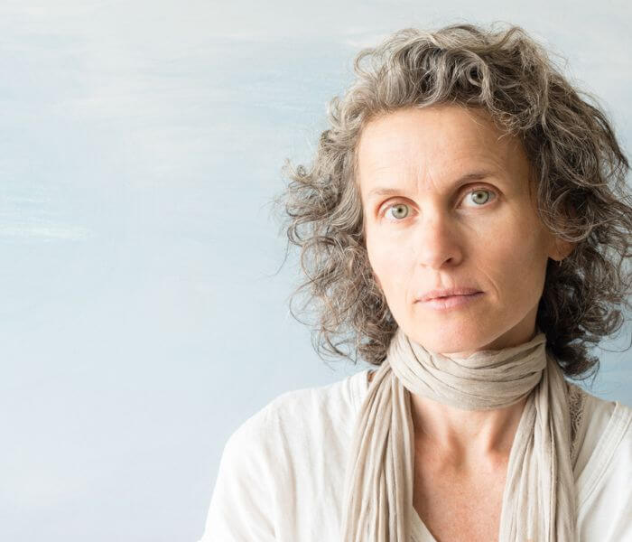 Portrait of middle aged woman with wavy grey hair and scarf against blue background